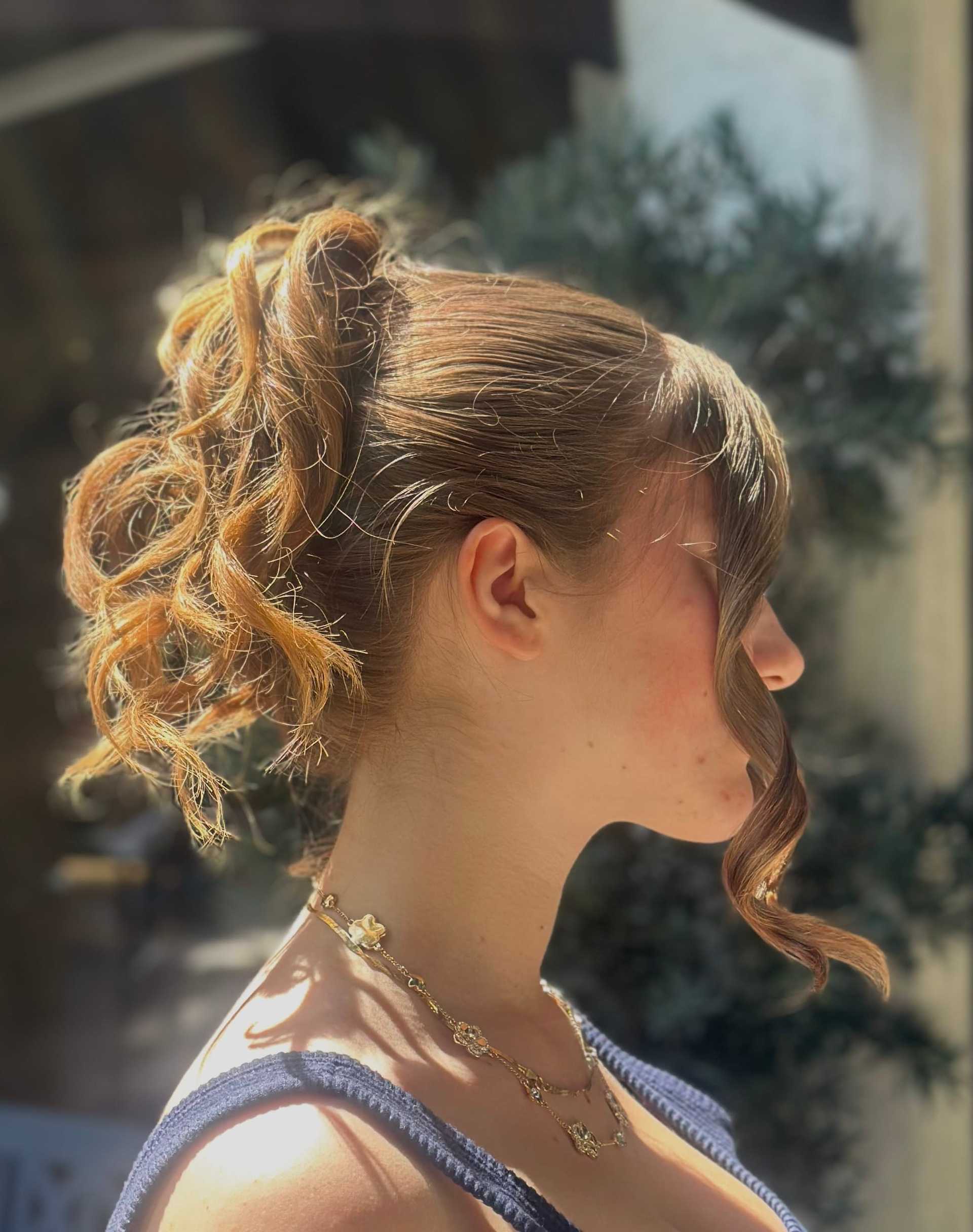 Profile of a woman with curly hair in a bright outdoor setting.