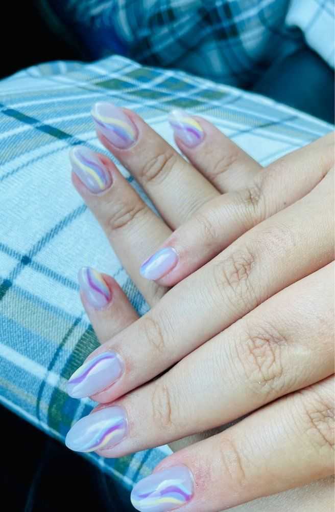 Hands with iridescent, pastel swirl nail art resting on plaid fabric.